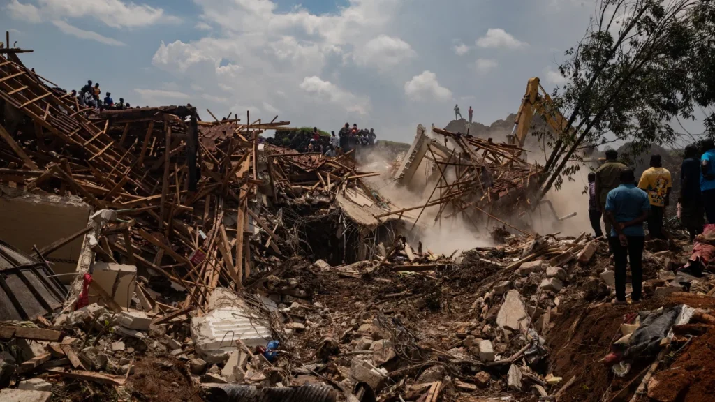 People look on as an excavator helps search for people trapped under debris after a landfill collapsed in Kampala