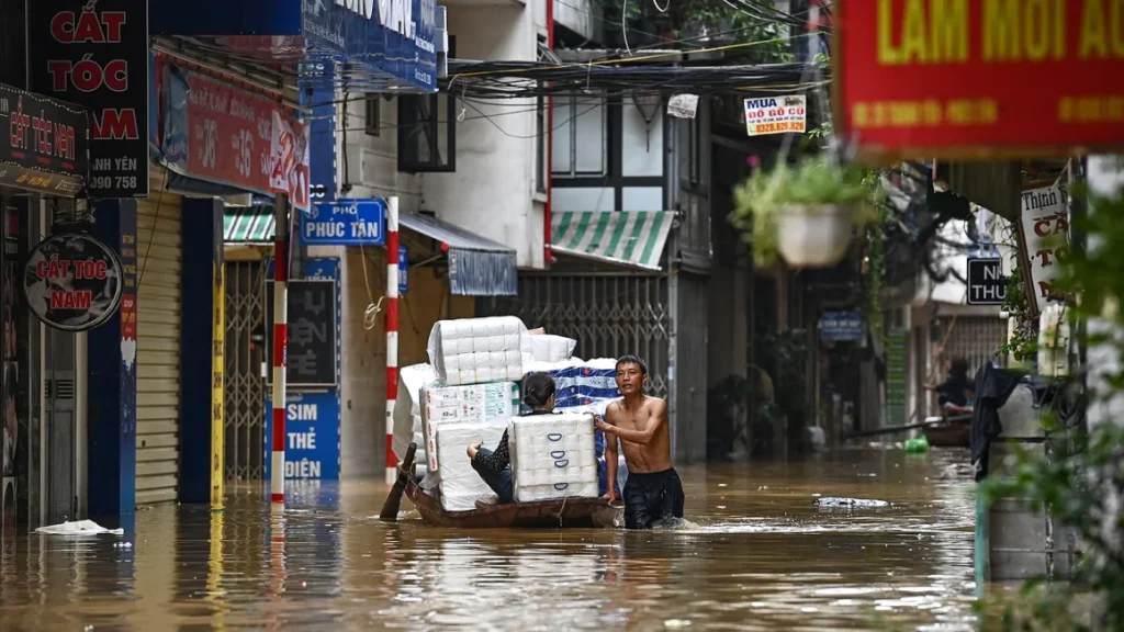 People transport basic commodities on a boat through flood waters on a street in Hanoi